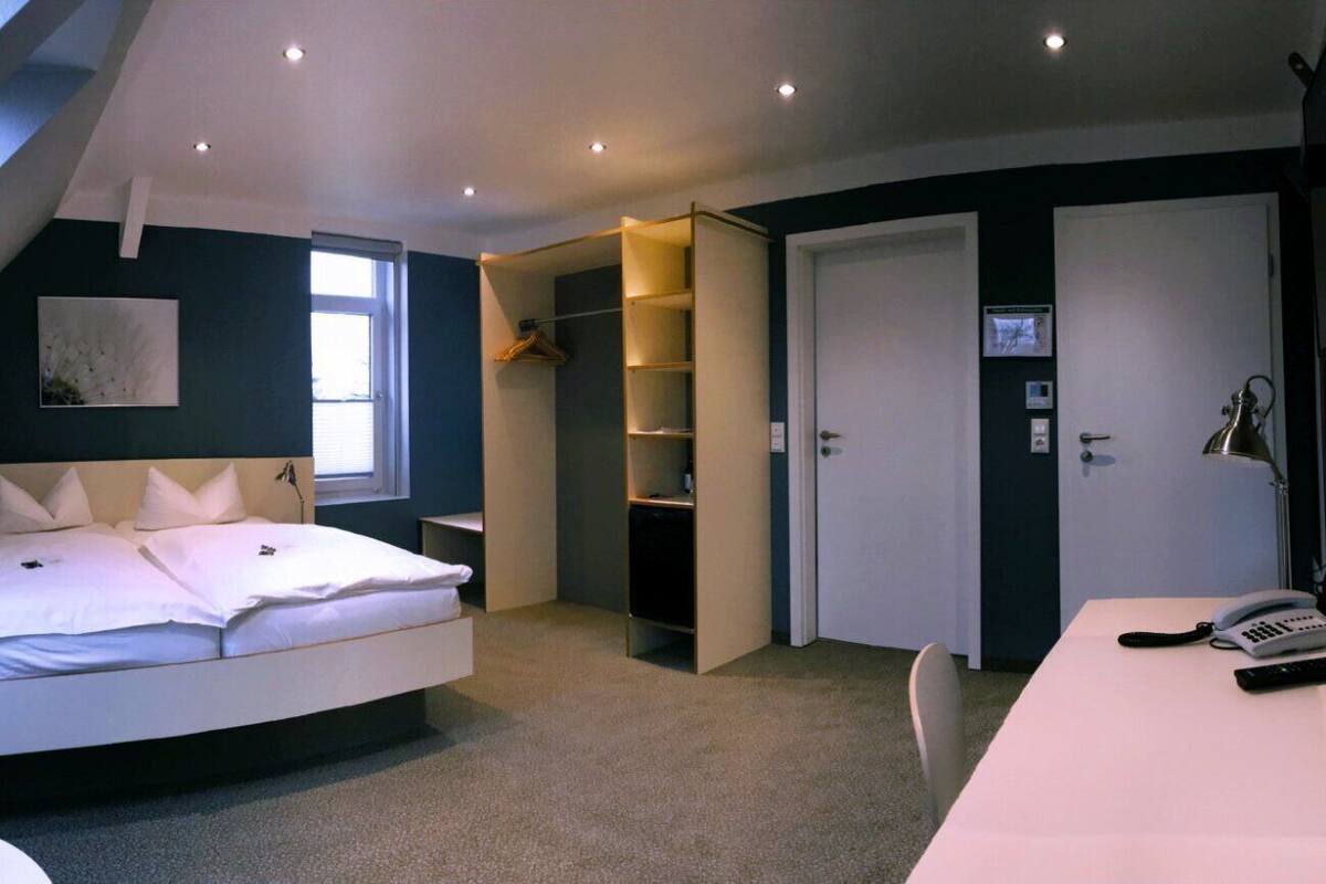 A bedroom with a bed, a desk, a telephone, and a wardrobe.