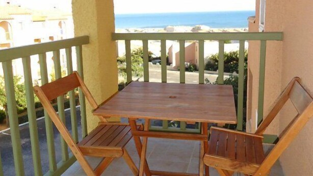 A wooden table and chairs on a balcony with a view of the sea.