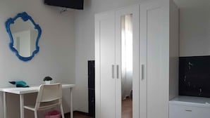 Une pièce comprenant un bureau blanc, une chaise, une petite plante en pot, un miroir à cadre bleu, une armoire blanche et un petit appareil électroménager blanc.