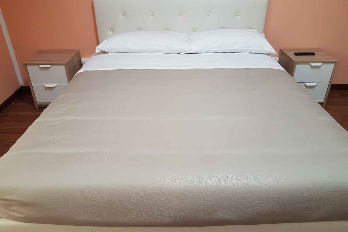 Ein ordentlich bezogenes Bett mit weißer Daunendecke, zwei Nachttische mit Schubladen und ein helles Kopfbrett.