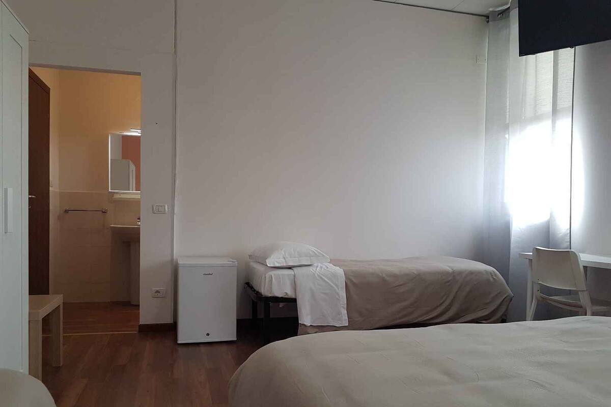 Ein Hotelzimmer mit zwei Betten, einem kleinen Nachttisch, einem Sessel und einem durch eine offene Tür einsehbaren Badezimmer.