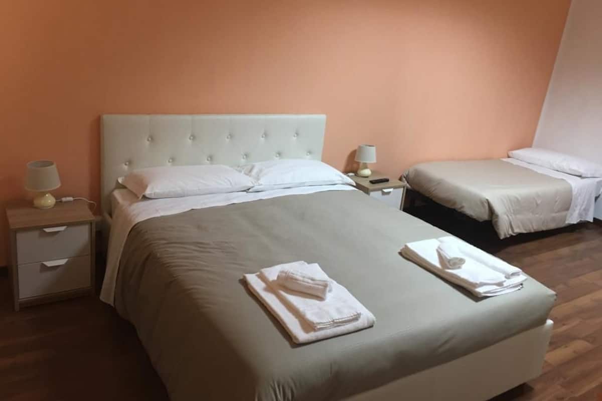 Ein Hotelzimmer mit einem großen Bett, zwei Nachttischen und einem kleineren Bett in der Ecke.