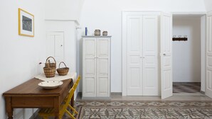 Un pasillo con una mesa de madera, cestas de mimbre, un armario blanco y un piso con baldosas.