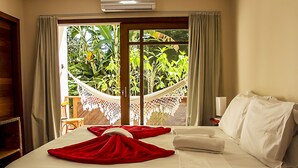 A hotel room with a bed, a hammock, and a view of greenery outside. - Pousada Timia (Cairu)