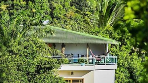 A two-story building with a green roof, surrounded by dense greenery. - Pousada Timia (Cairu)