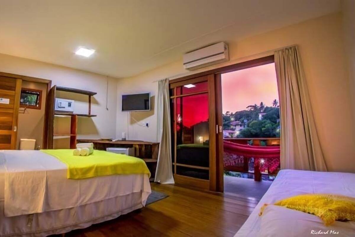 A hotel room with two beds, a TV, a desk, and a balcony with a view.