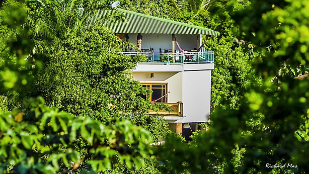 A two-story building with a green roof, surrounded by dense foliage. - Pousada Timia (Cairu)