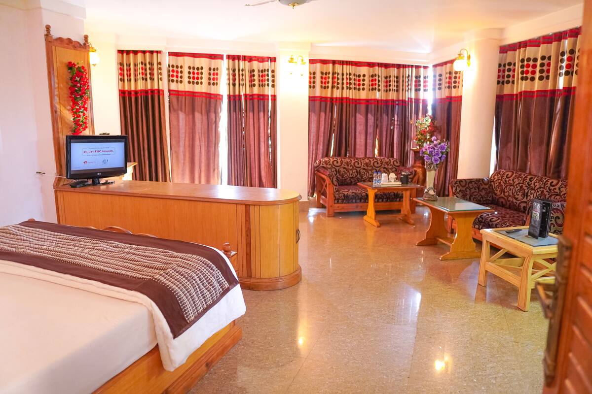 A hotel room with a bed, a sofa, a coffee table, a TV, and curtains.