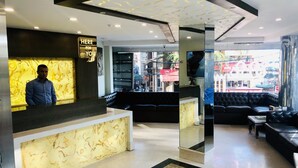 Un hall d’hôtel moderne doté d’un comptoir d’accueil, d’un espace salon et de grandes fenêtres donnant sur la rue.