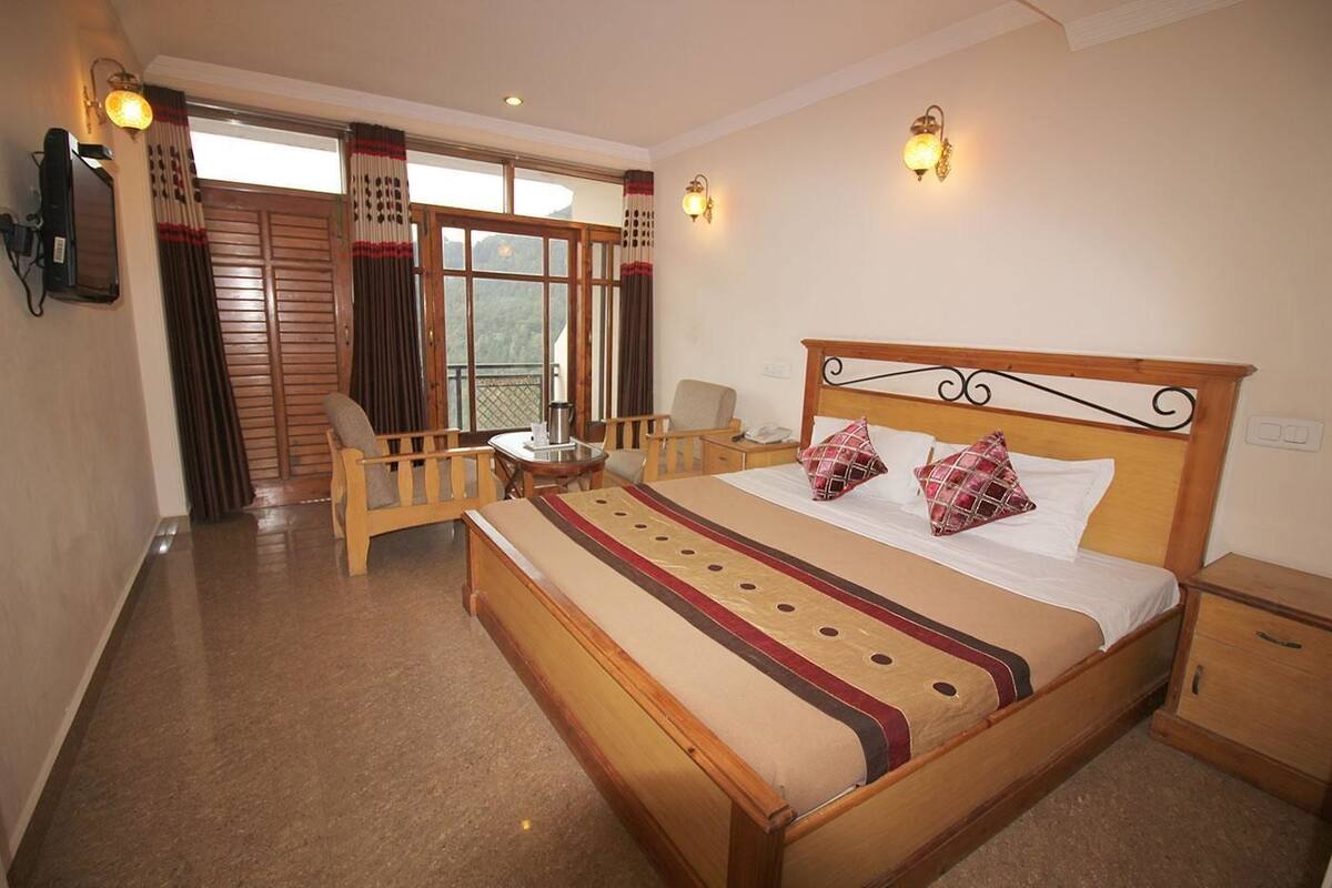 A hotel room with a wooden bed, a desk, a chair, and a balcony with curtains.