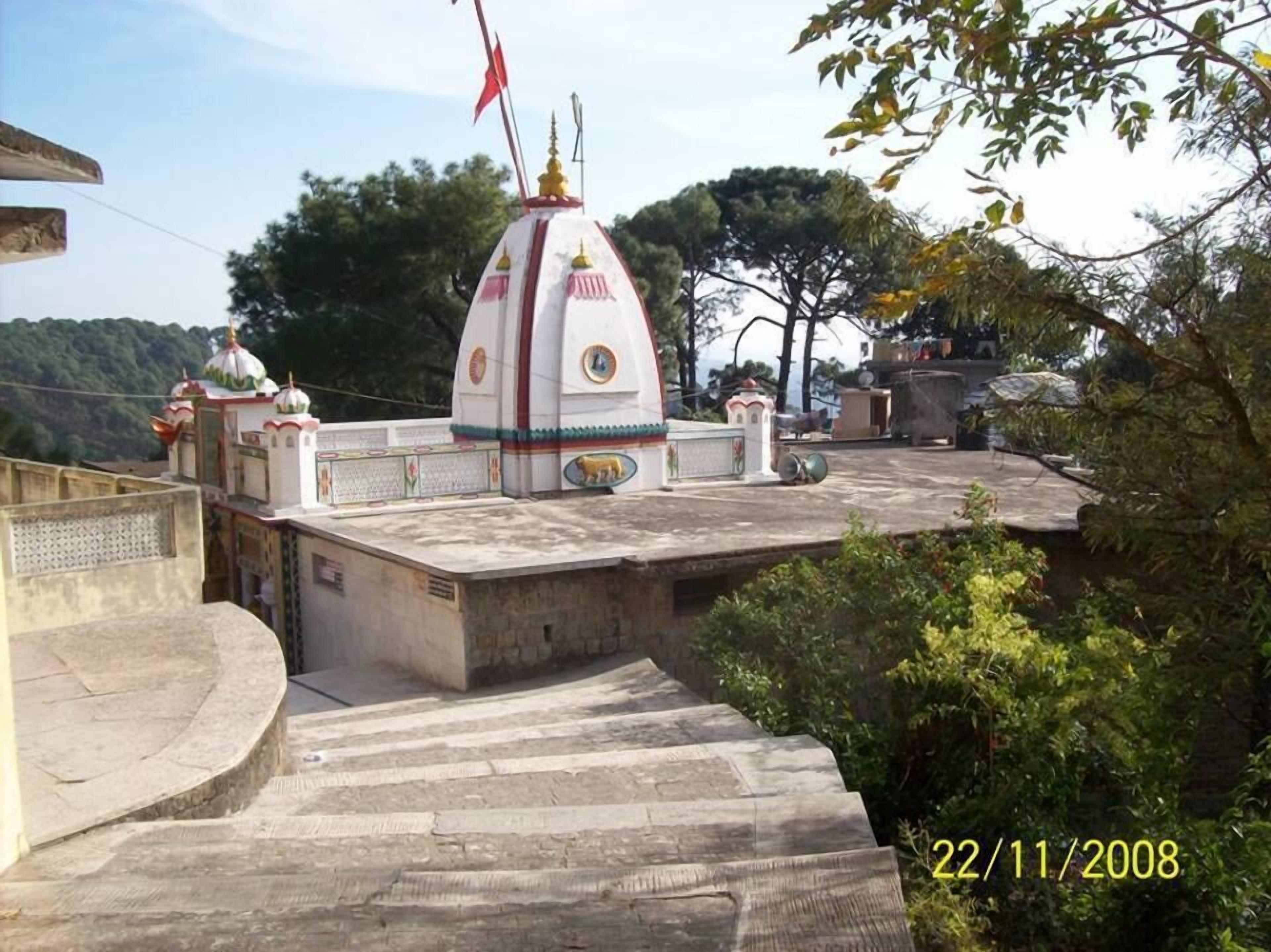 Ein Tempel mit einer weißen Kuppel und einer roten Flagge, umgeben von Bäumen und einer Treppe.