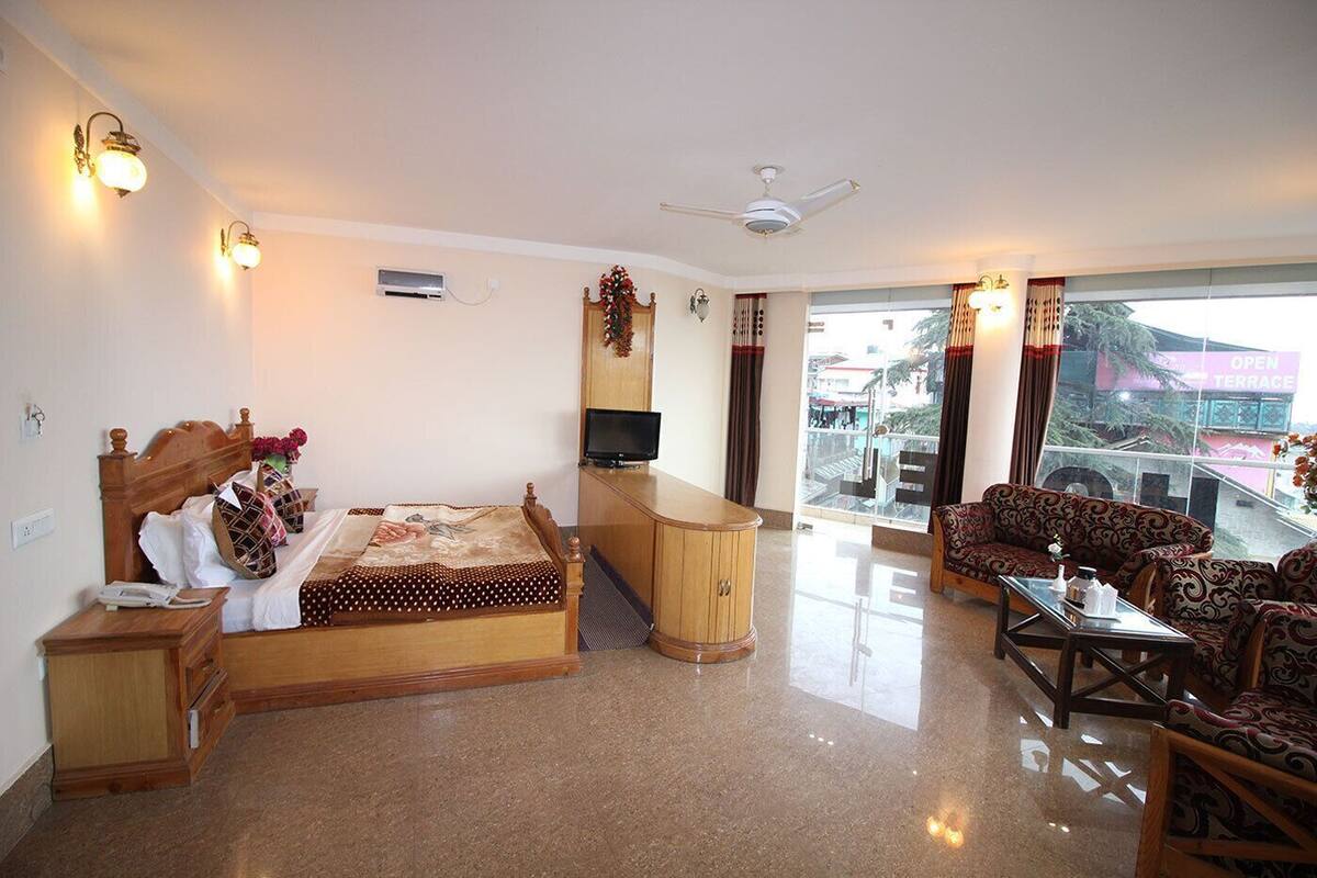 A hotel room with a bed, a TV, a desk, a sofa, and a balcony with a view.