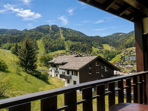 A mountain cabin with a wooden deck, surrounded by lush greenery and a clear view of the valley below.