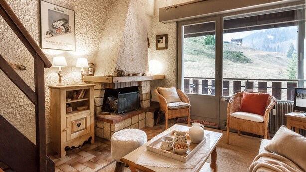 A cozy living room with a fireplace, wooden furniture, and a view of a mountainous landscape.