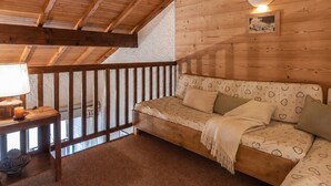 A cozy wooden cabin interior with a wooden ceiling, a sofa with patterned cushions, a small table with a lamp, and a framed picture on the wall.