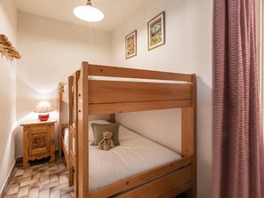 Una cama litera con un oso de peluche en la cama inferior, una mesita de noche pequeña con una lámpara y un tapiz de pared estampado.