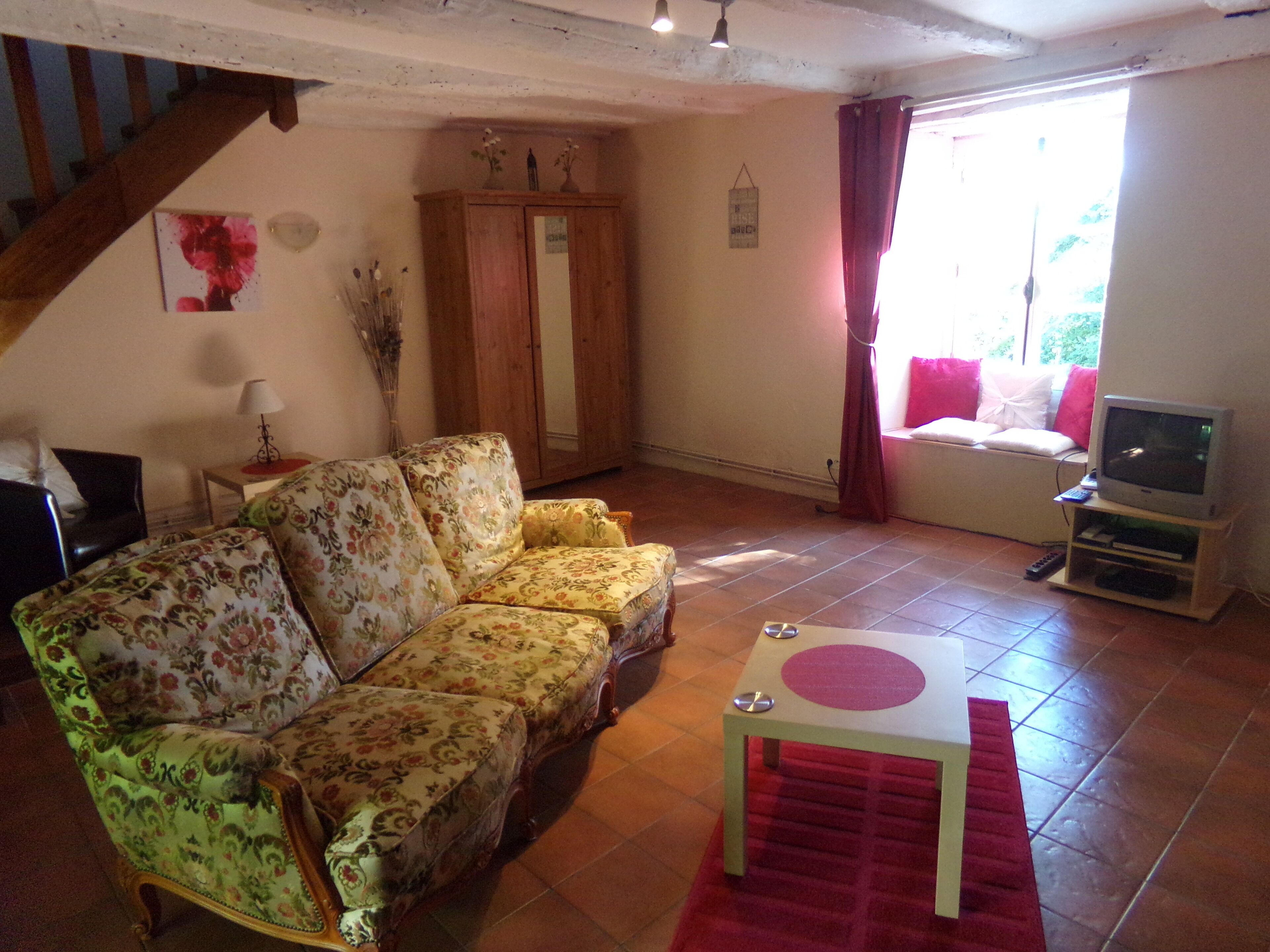 A living room with a floral sofa, a wooden cabinet, a television, and a red rug.