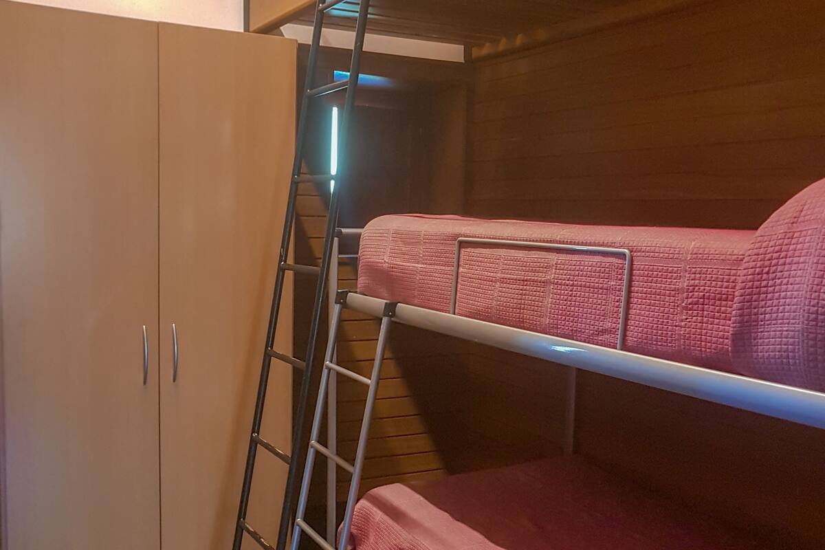 En våningssäng med en stege, en garderob och ett klinkergolv.