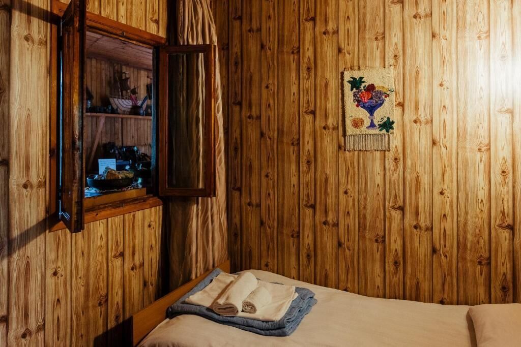 Habitación con paneles de madera, una cama, una ventana con cortinas y un pequeño estante con objetos.