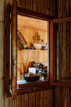 Ein Holzinnenraum mit einem Fenster, das einen Raum mit einem Tisch, einer Schüssel und einem Stuhl zeigt.