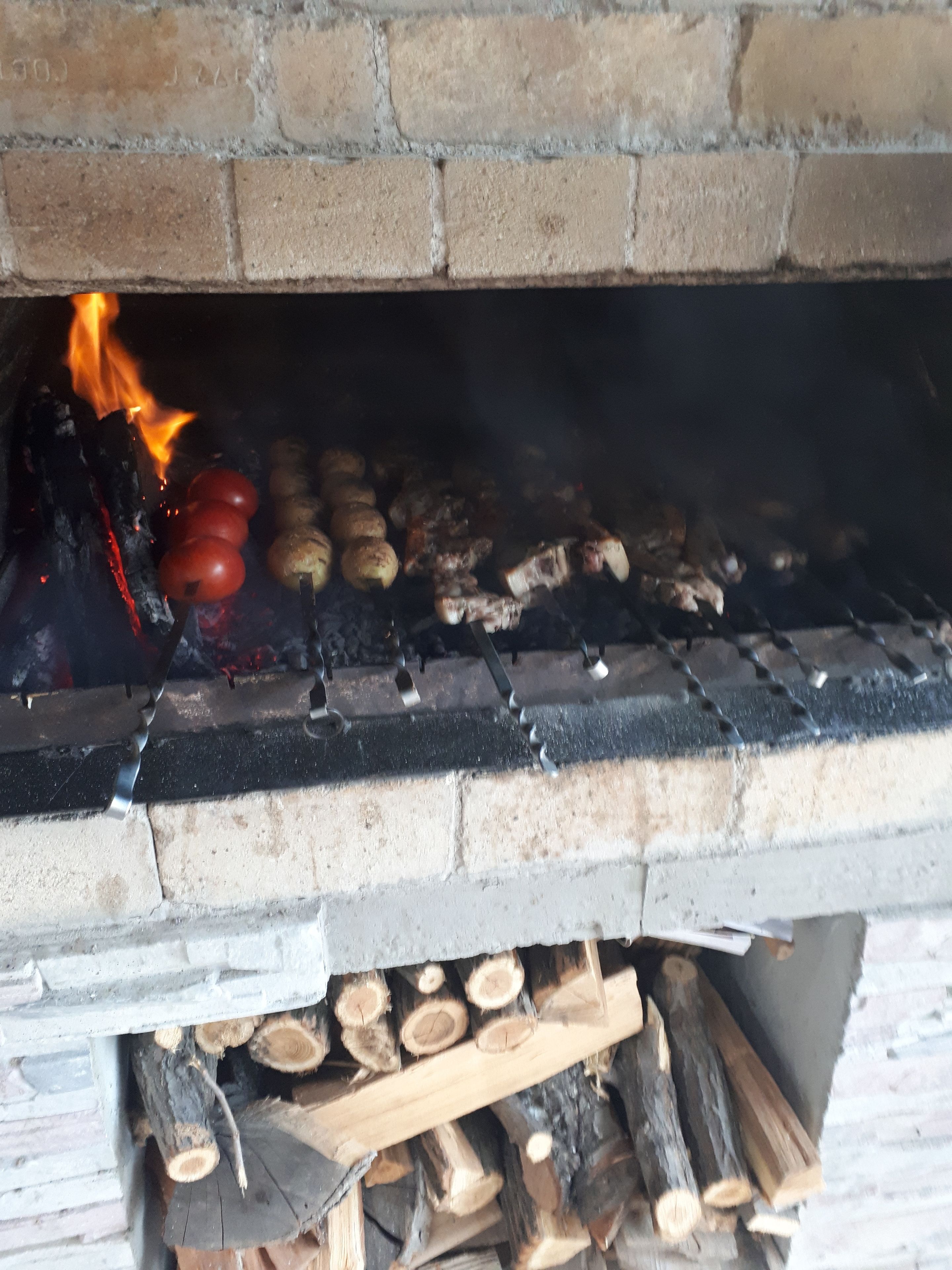 Lareira a lenha com lenha e alimentos como tomates e batatas sendo cozidos.