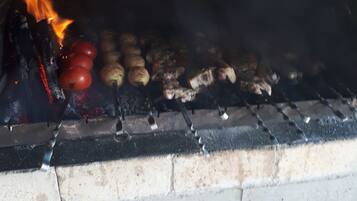 Lareira a lenha com lenha e alimentos como tomates e batatas sendo cozidos.