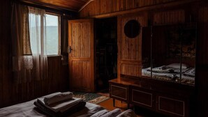 Una habitación tenuemente iluminada, con paredes de madera y un armario grande. Hay una cama con mantas dobladas y una mesita de noche con una lámpara.