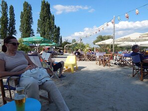 Un espace extérieur aménagé avec des tables et des chaises, situé au bord de la plage, entouré de verdure et ombragé par des parasols.