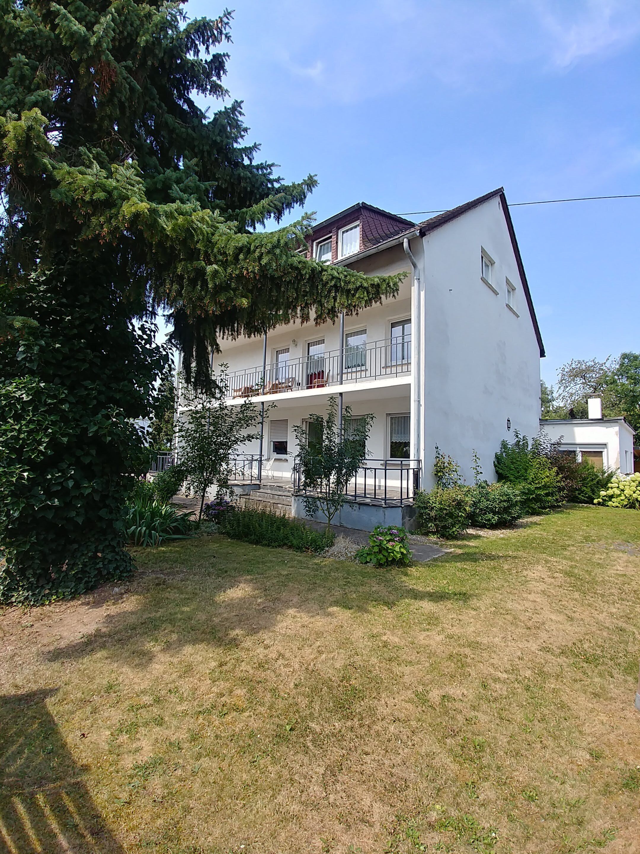 A two-story building with a white exterior, a red roof, and a balcony on the upper floor.
