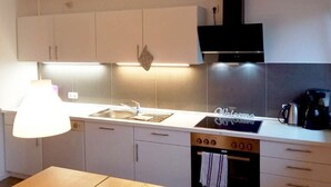 Una cuina moderna amb armaris blancs, una campana extractora negra, forn integrat i una cafetera.