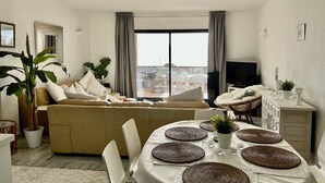 Una sala de estar moderna con un sofá, una mesa de comedor y sillas, un televisor y vistas al balcón.