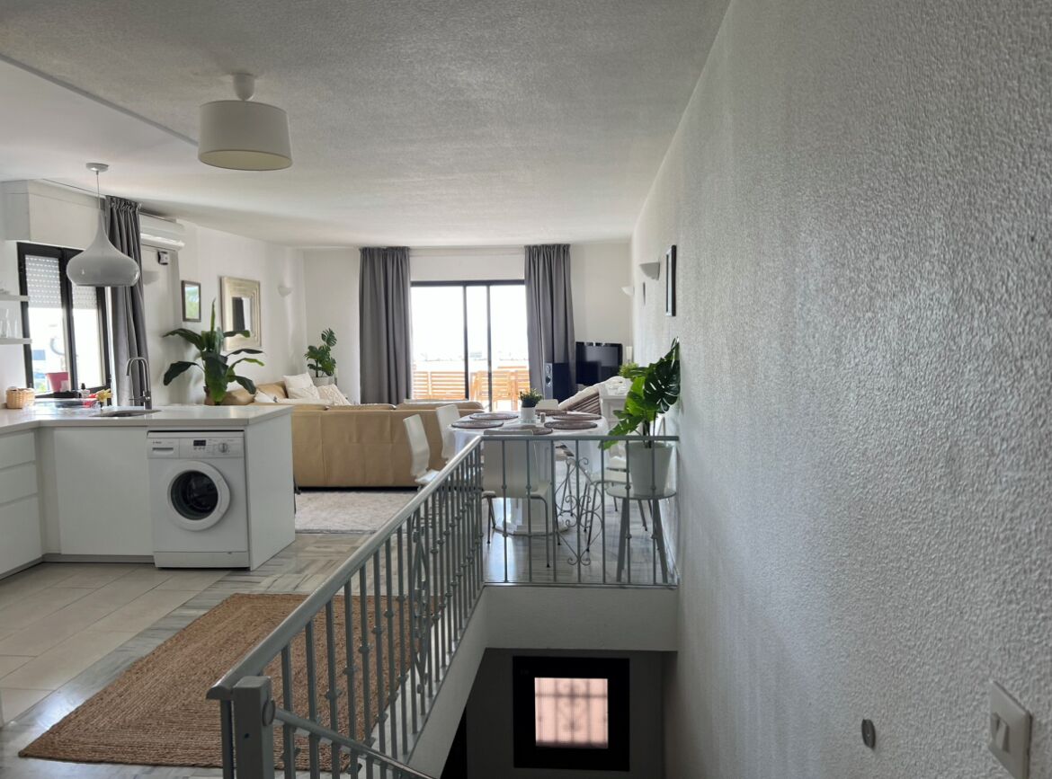 Un apartamento moderno con cocina, comedor y sala de estar. Incluye lavadora, mesa de comedor con sillas y sofá.