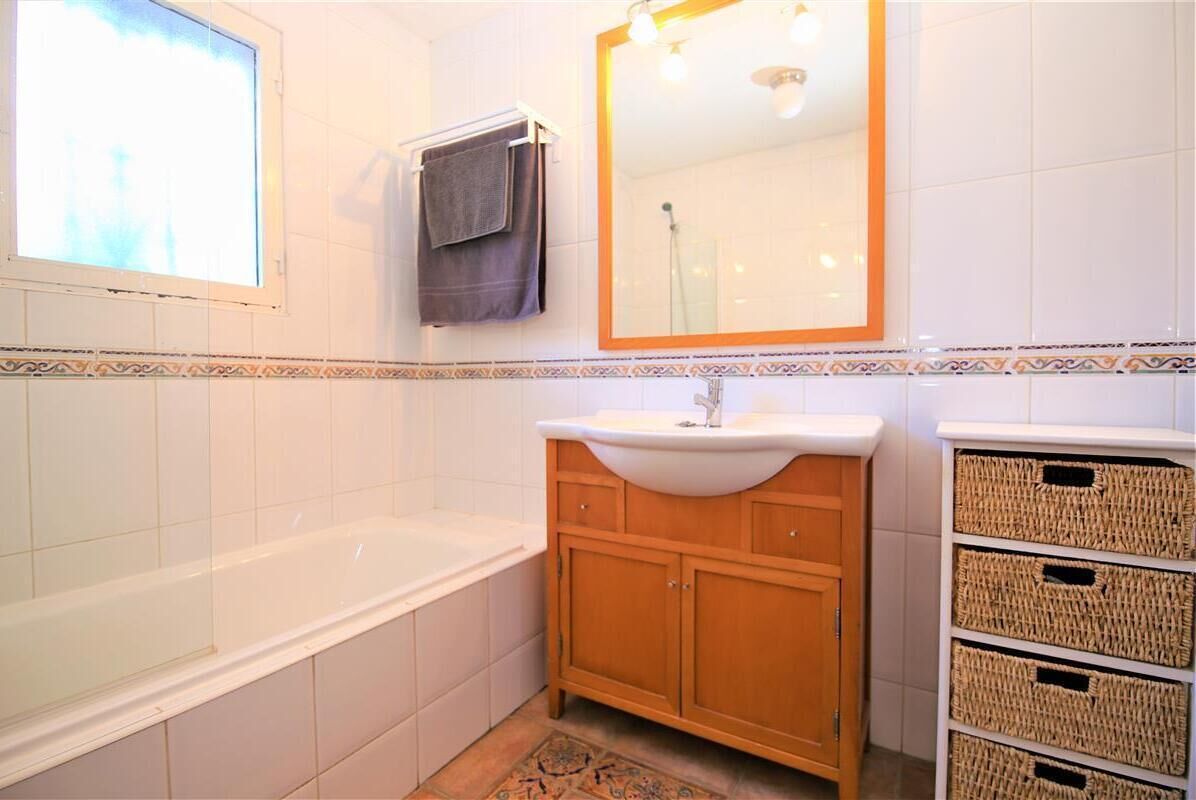 Un baño con bañera, lavabo con espejo y cestas de mimbre en un armario.