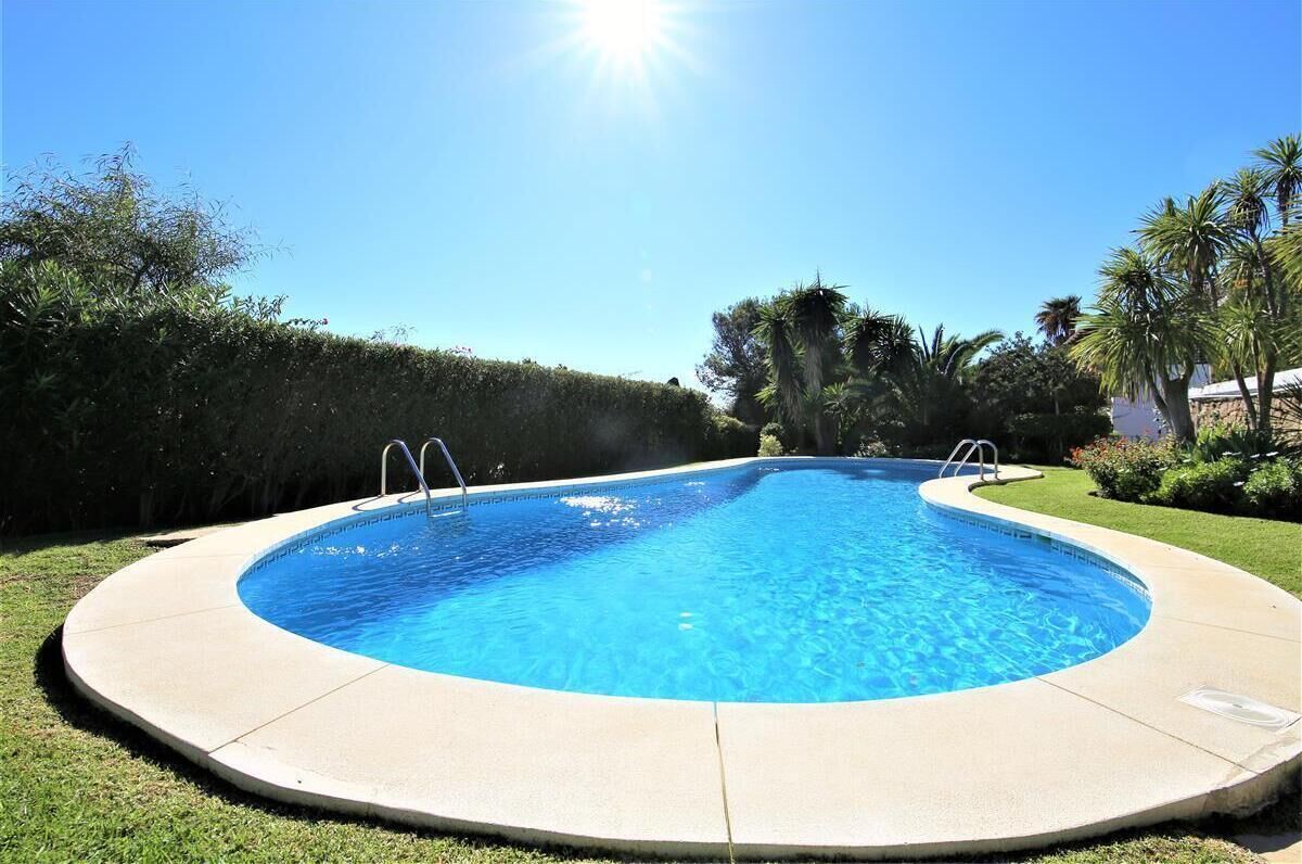 A round swimming pool with a clear blue water surface, surrounded by a concrete deck and a well-maintained lawn.