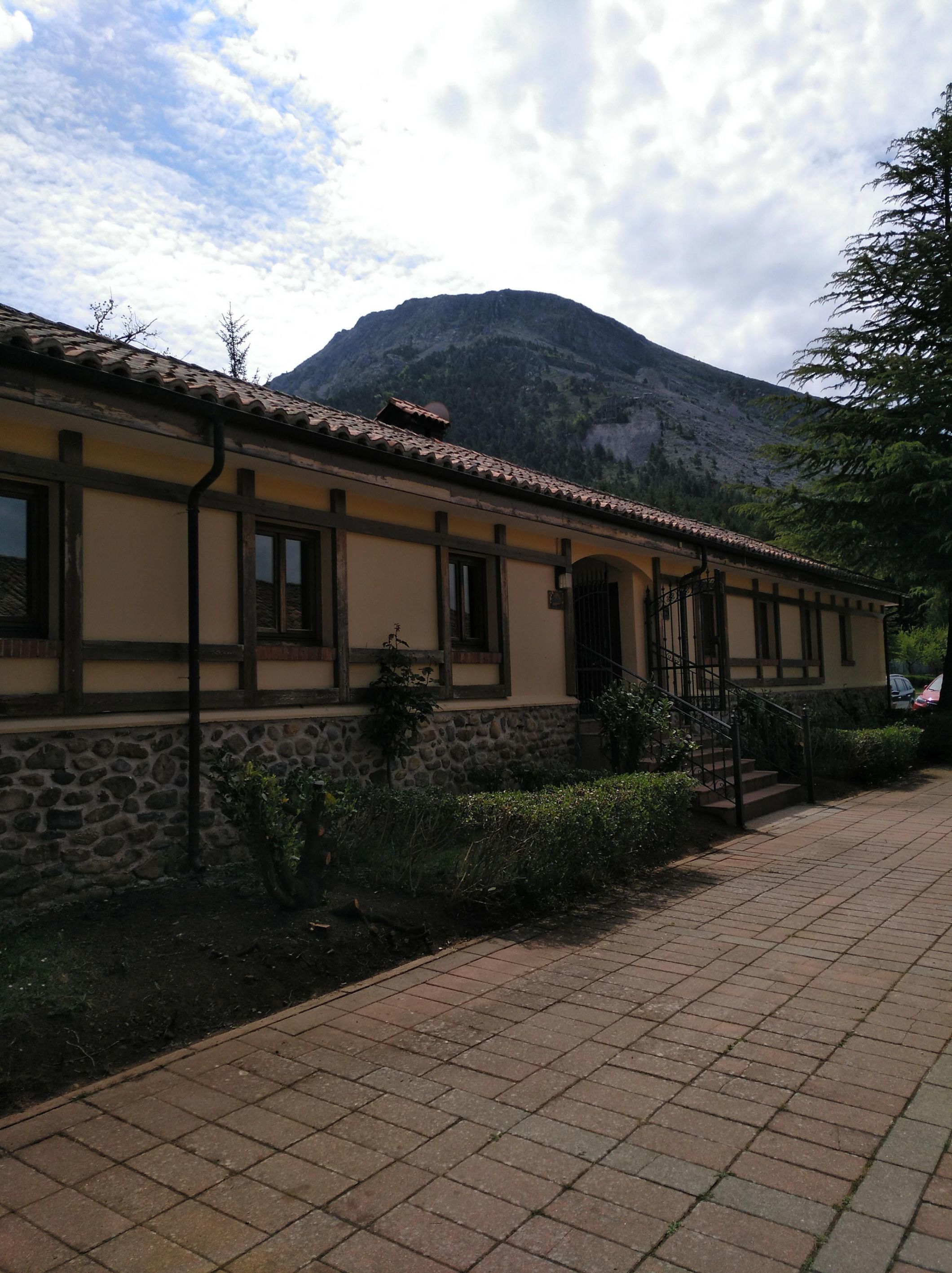 A building with a stone facade and a tiled roof, a staircase, and a mountain in the background.