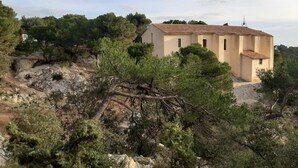 Un edificio de una sola planta con techo plano, rodeado de árboles y terreno rocoso.