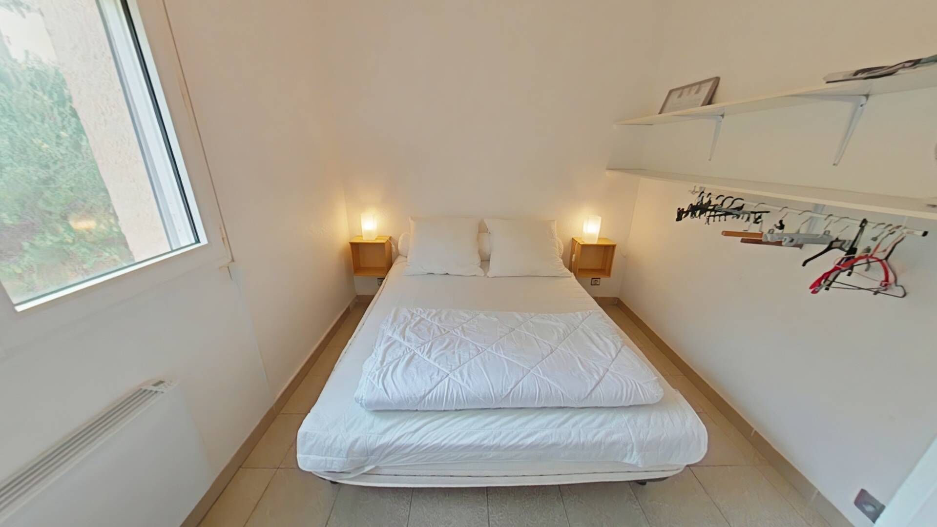 A small, well-lit bedroom with a bed, bedside lamps, and a wall-mounted bike rack.