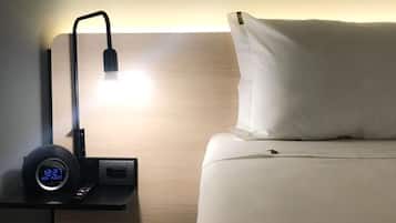 Una cama bien hecha con una almohada y una mesita de noche con un reloj digital y una lámpara.