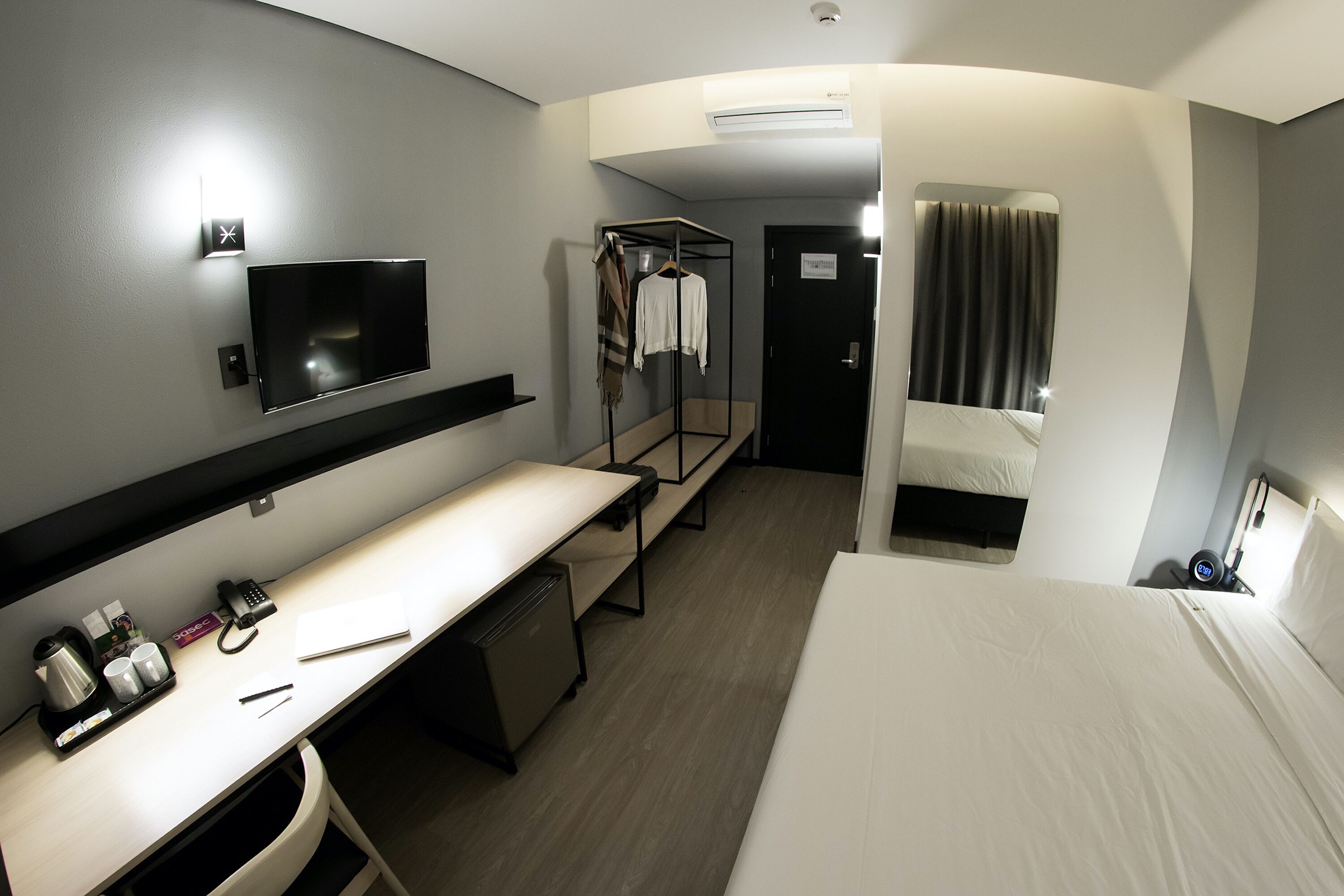 Hotelkamer met een bed, bureau met computer, televisie, kledingkast en spiegel.