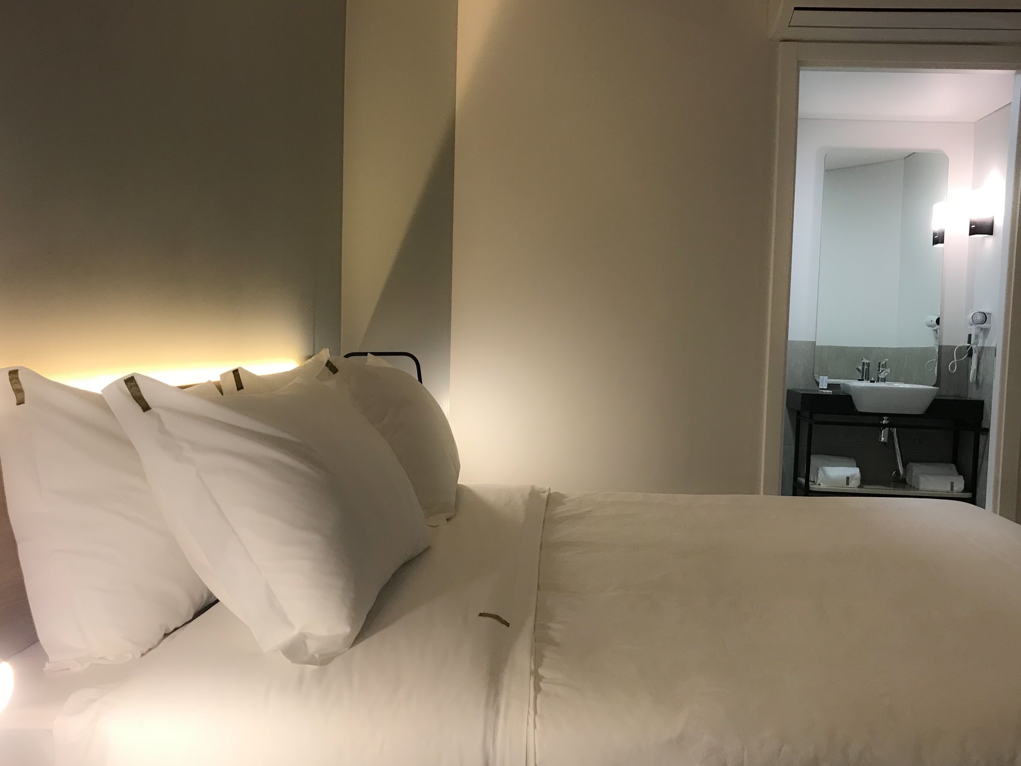 A hotel room with a neatly made bed, a bedside table, and a bathroom visible through an open door.