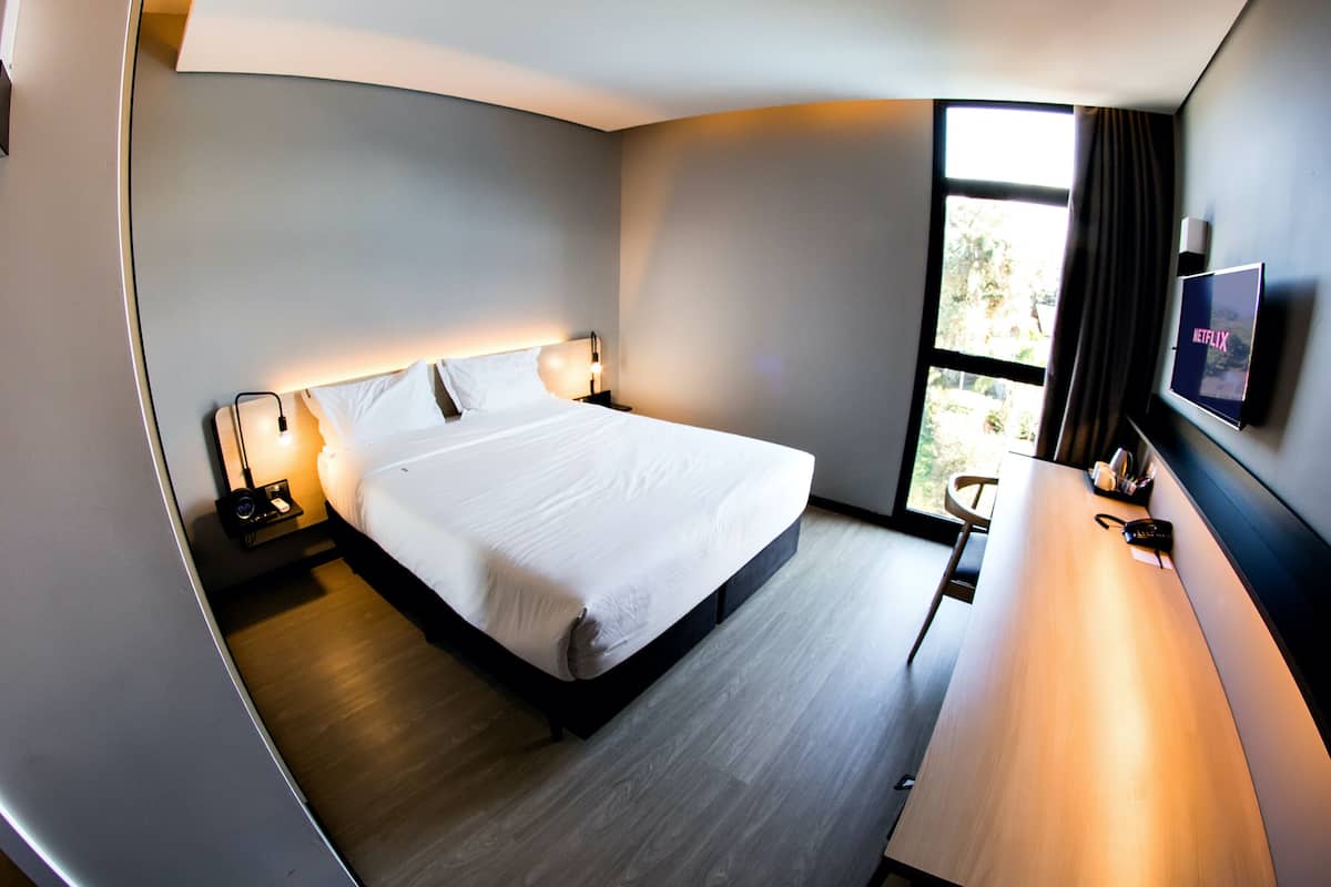 Een moderne hotelkamer met een groot bed, bedlampjes, een bureau en een televisie waarop 'NETFLIX' wordt weergegeven.