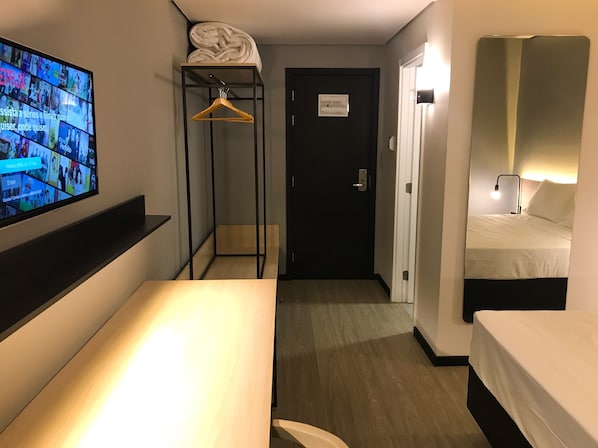 A hotel room with a bed, a TV mounted on the wall, a wooden floor, a door, and a small closet with a hanging rack. - Naalt Hotel Joinville (Joinville)