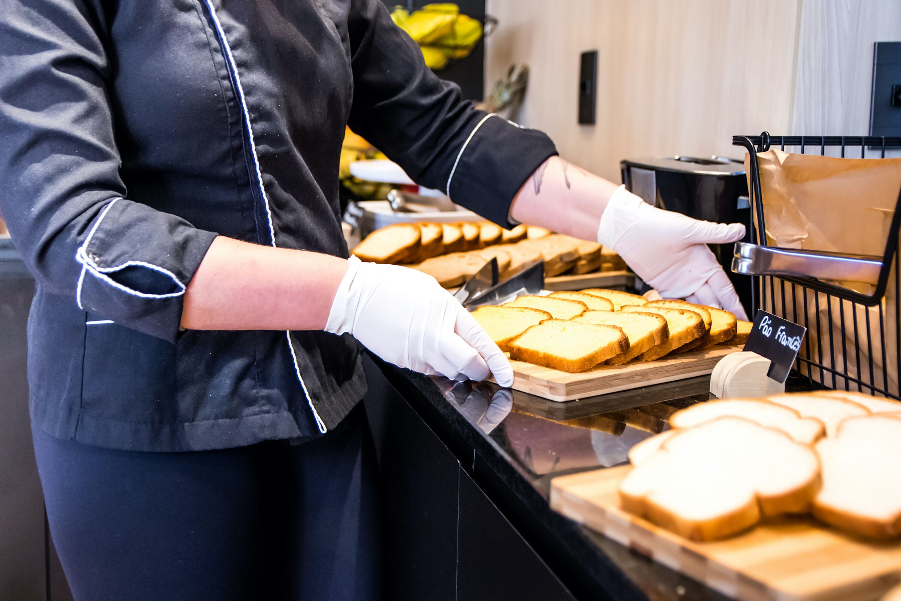A person in a black uniform with white gloves preparing sliced bread on a counter.