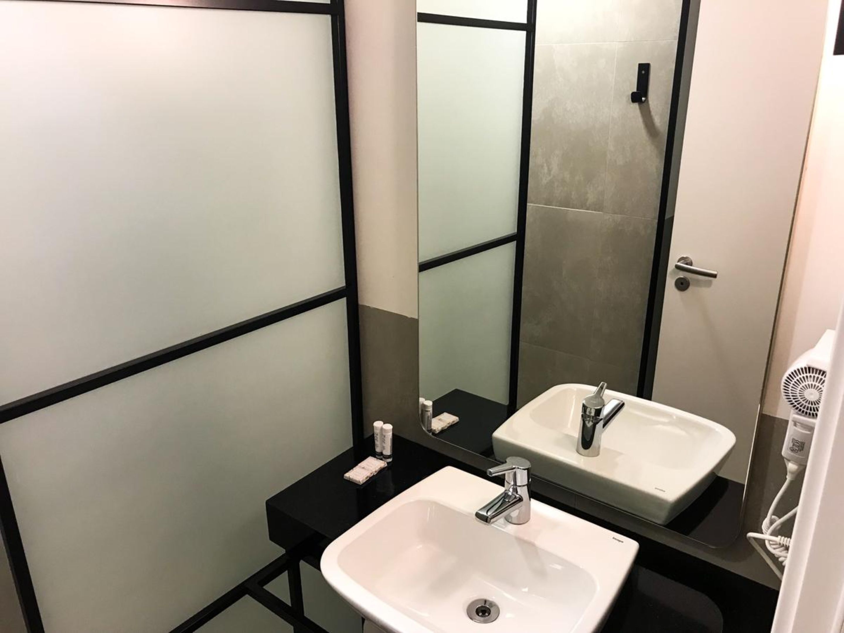 A modern bathroom with a white sink, a large mirror, and a hairdryer.