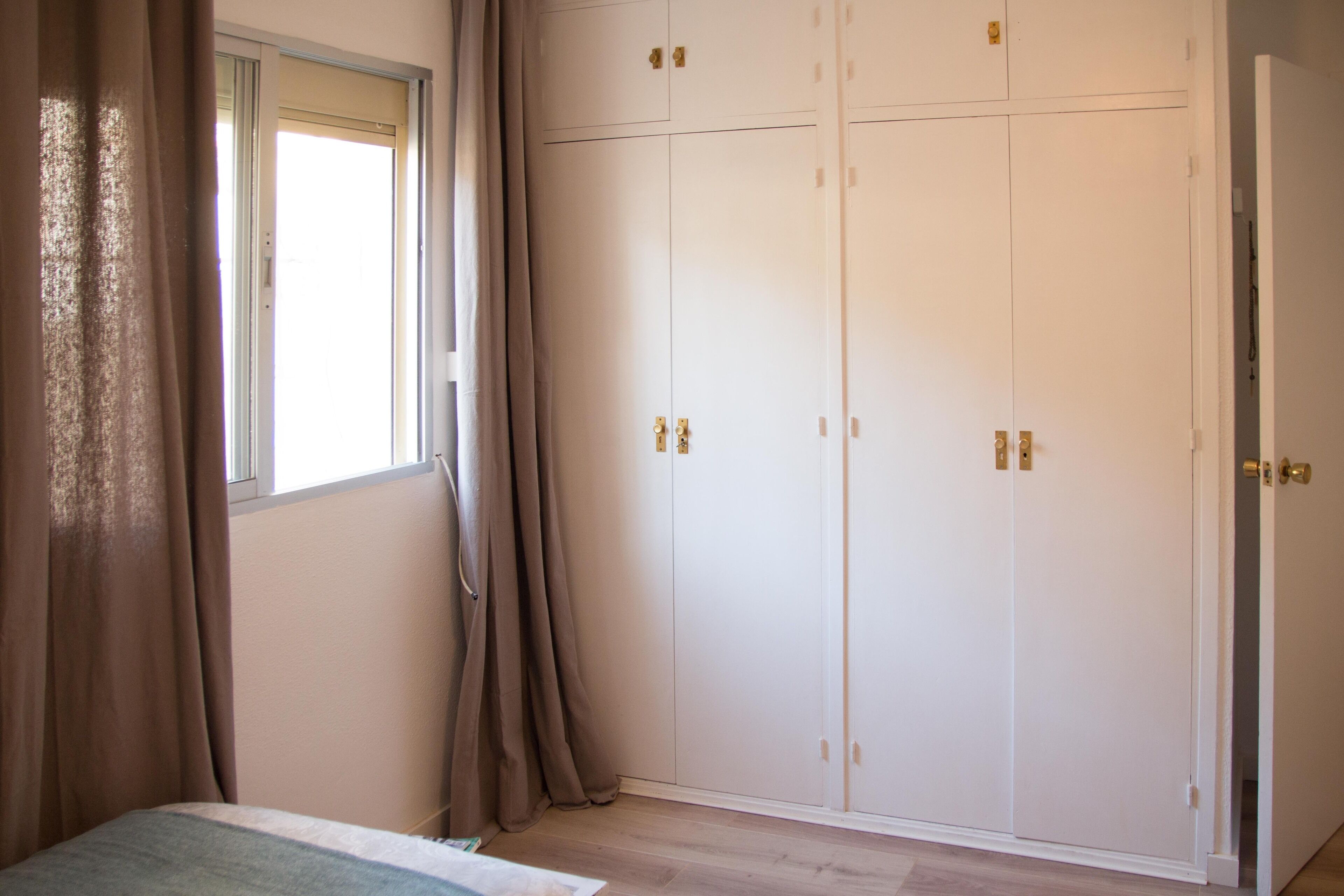 A bedroom with a bed, a wardrobe, and a window with curtains.