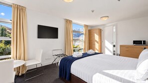A hotel room with a bed, a desk, a chair, a TV, and a view of mountains.