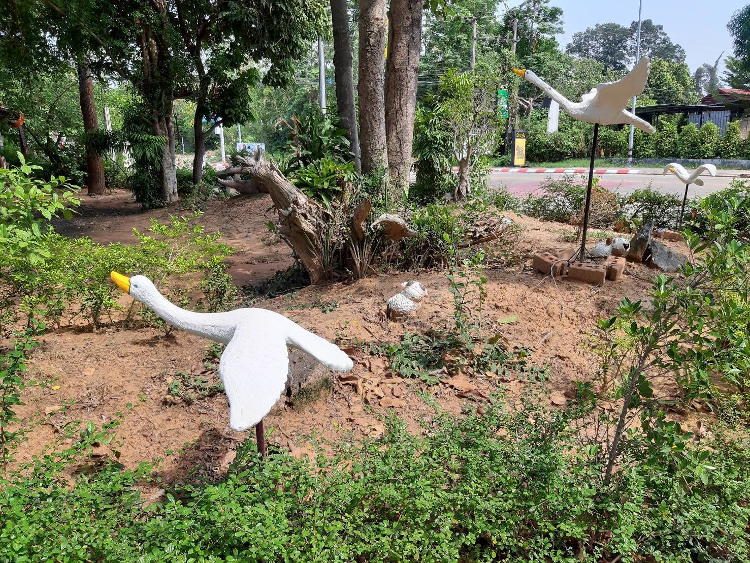 A naturalistic garden with sculptures of a swan and a sheep amidst trees and shrubs.