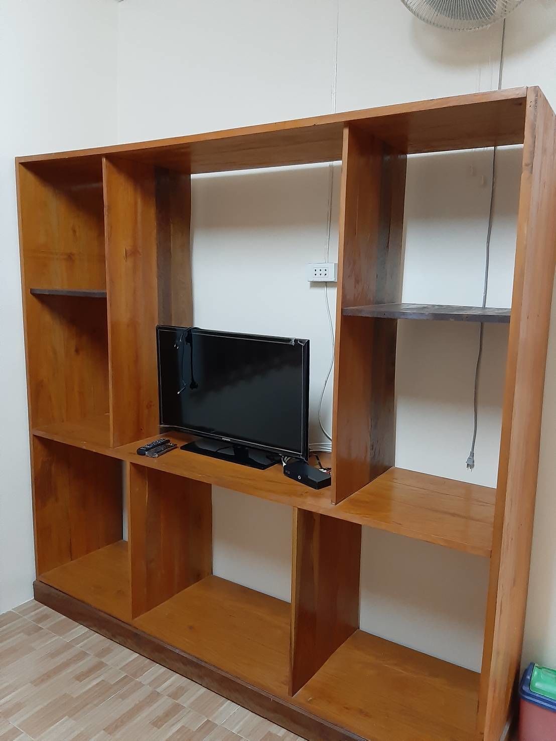 Un mueble de madera para televisor con televisor de pantalla plana, controles remotos y cable de alimentación.