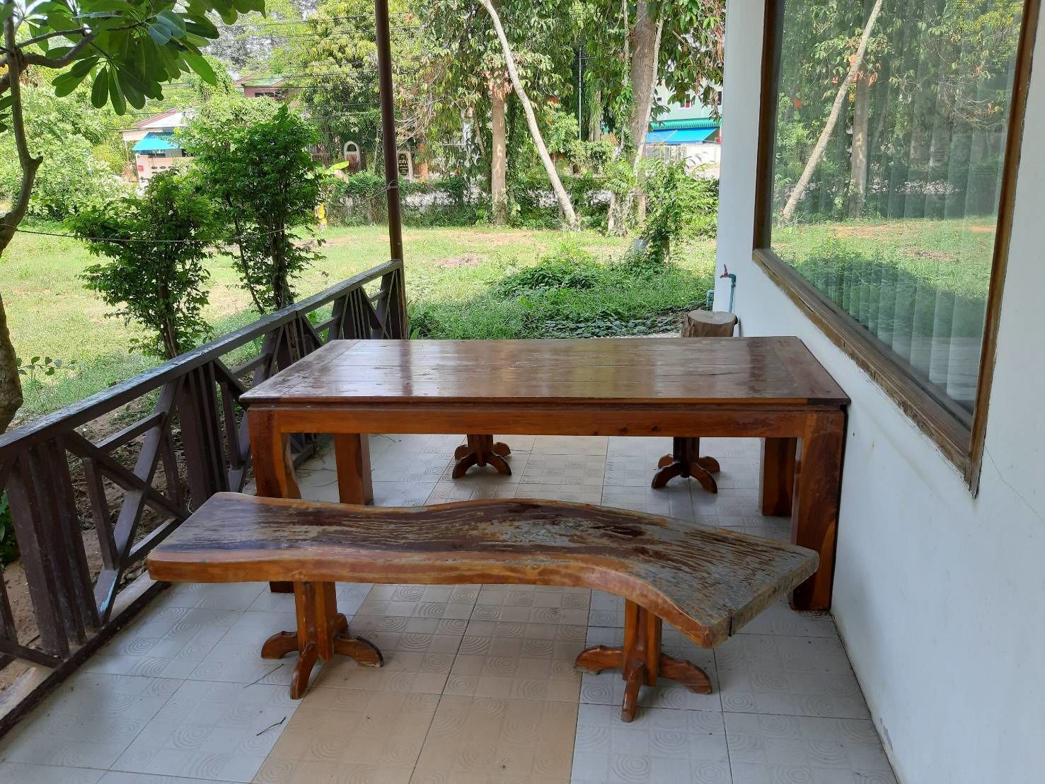 A wooden table and bench in a covered outdoor area with a view of greenery and buildings in the background.