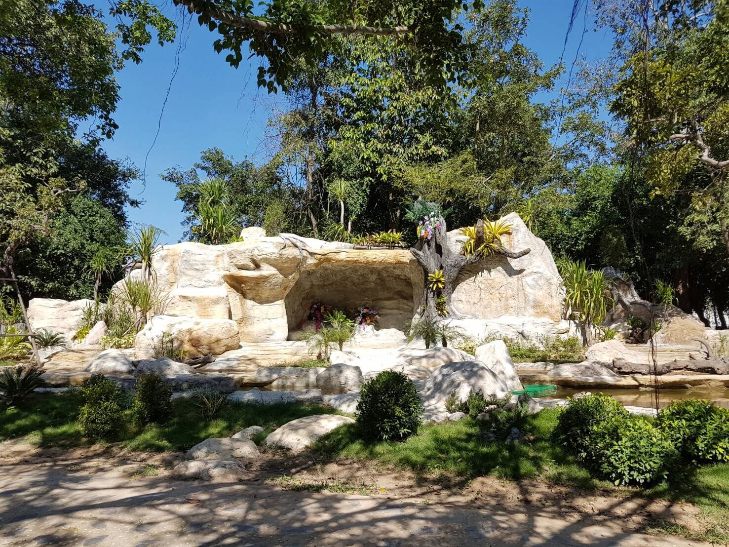 A naturalistic rock formation with a small cave and surrounding vegetation.